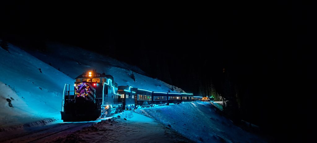 train at night with blue Christmas light on in the snow.