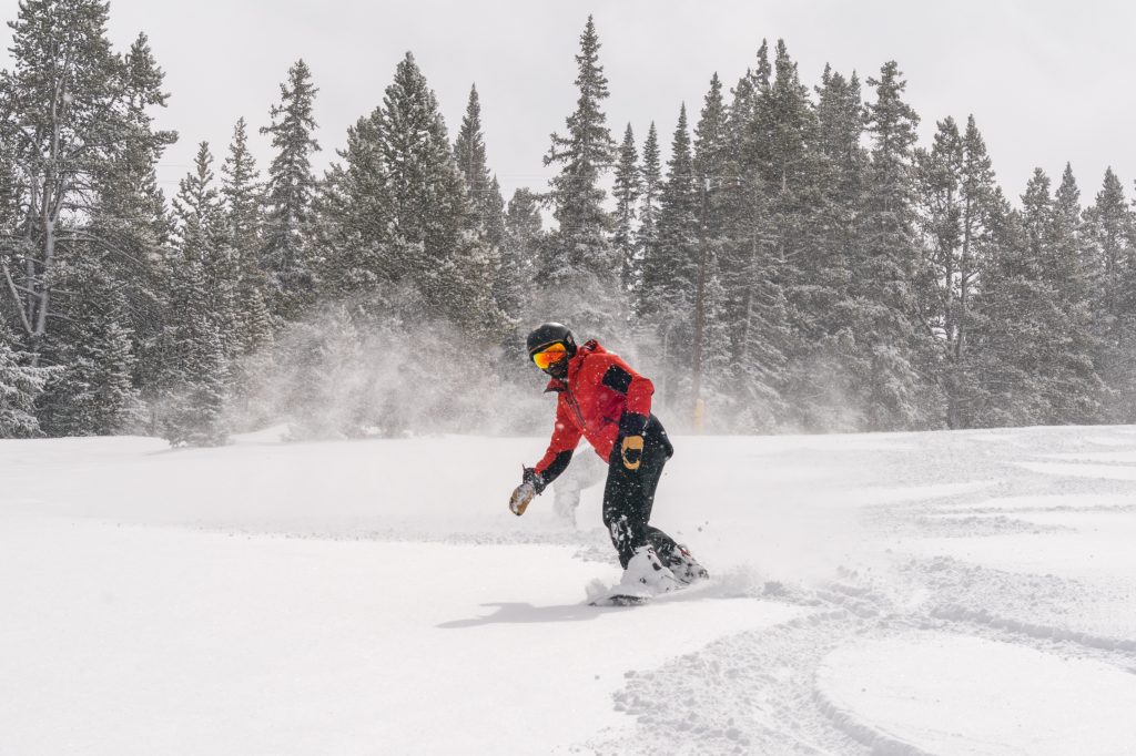 A snowboarder in a red jacket riding fresh snow at Ski Cooper