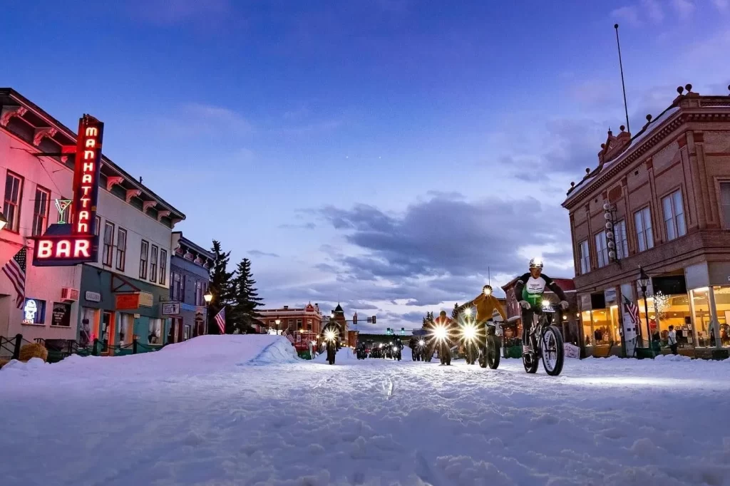 people biking down main street in the snow.
