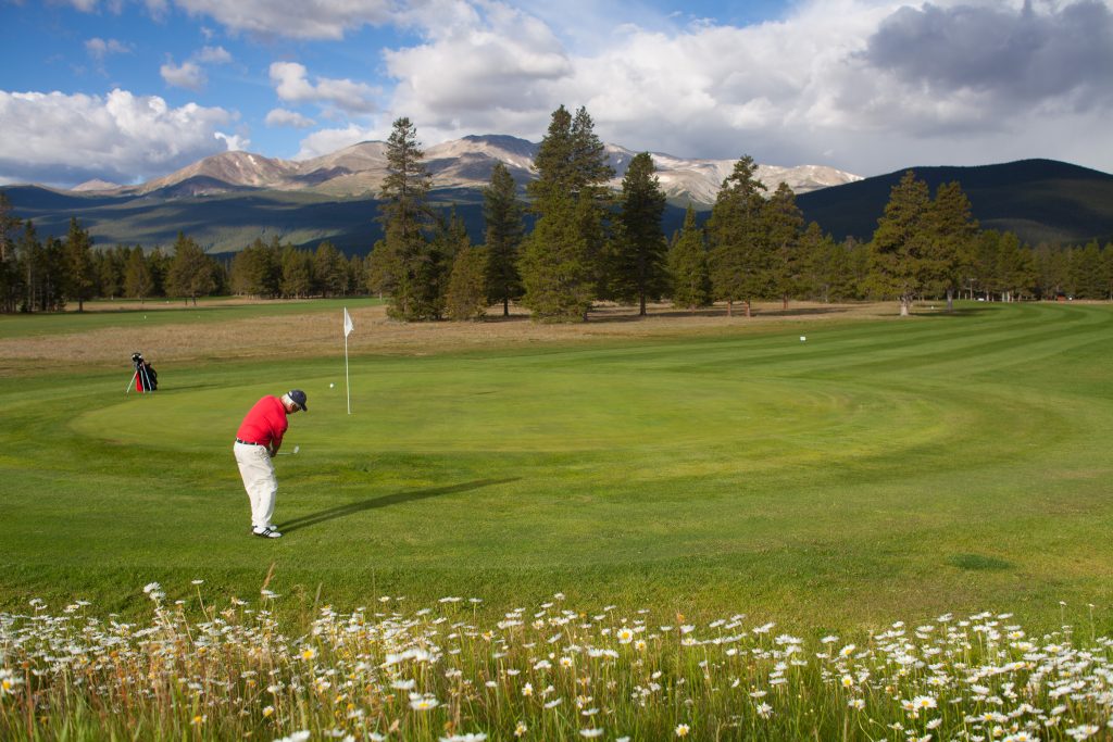 man playing golf with mountains in the background.