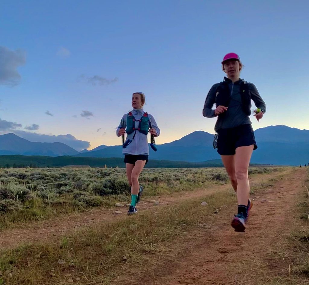 Two female runners on wide dirt trail at dusk with a mountain backdrop