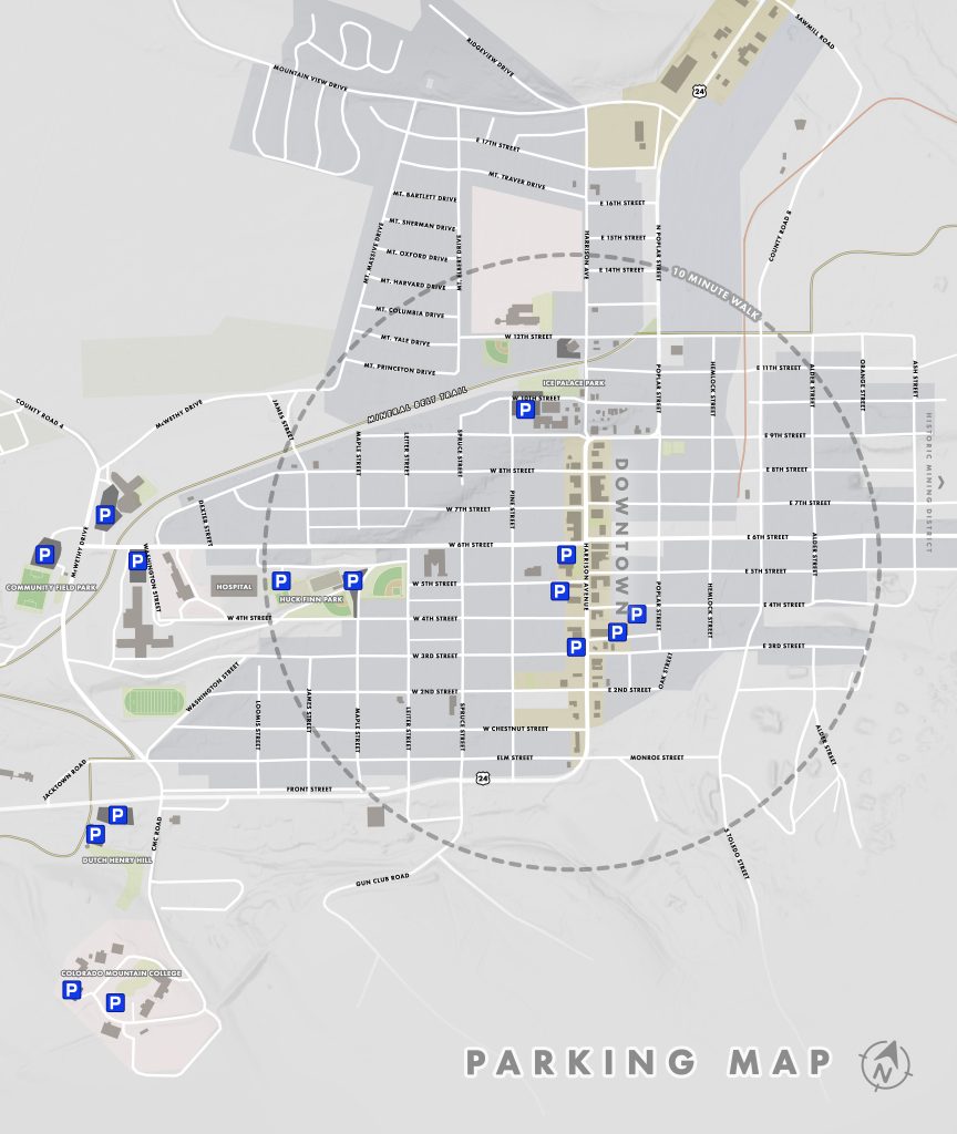 Map showing a city layout with labeled streets. Blue "P" icons indicate parking locations, mainly around the downtown area. A dashed circle highlights a central zone.