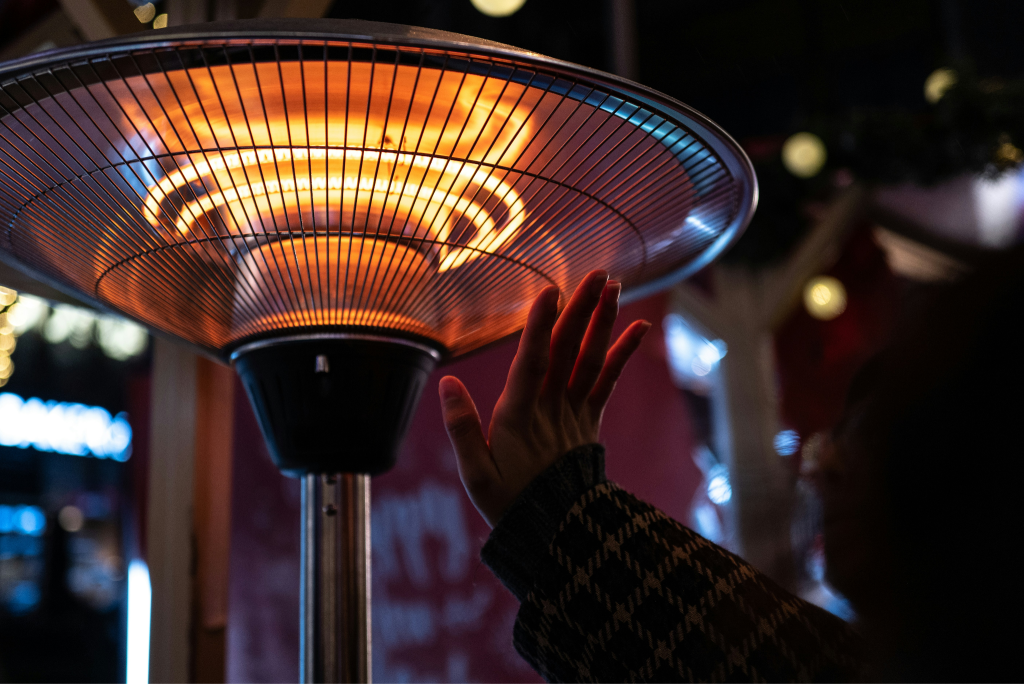 Hand reaching toward a glowing portable outdoor heater at night